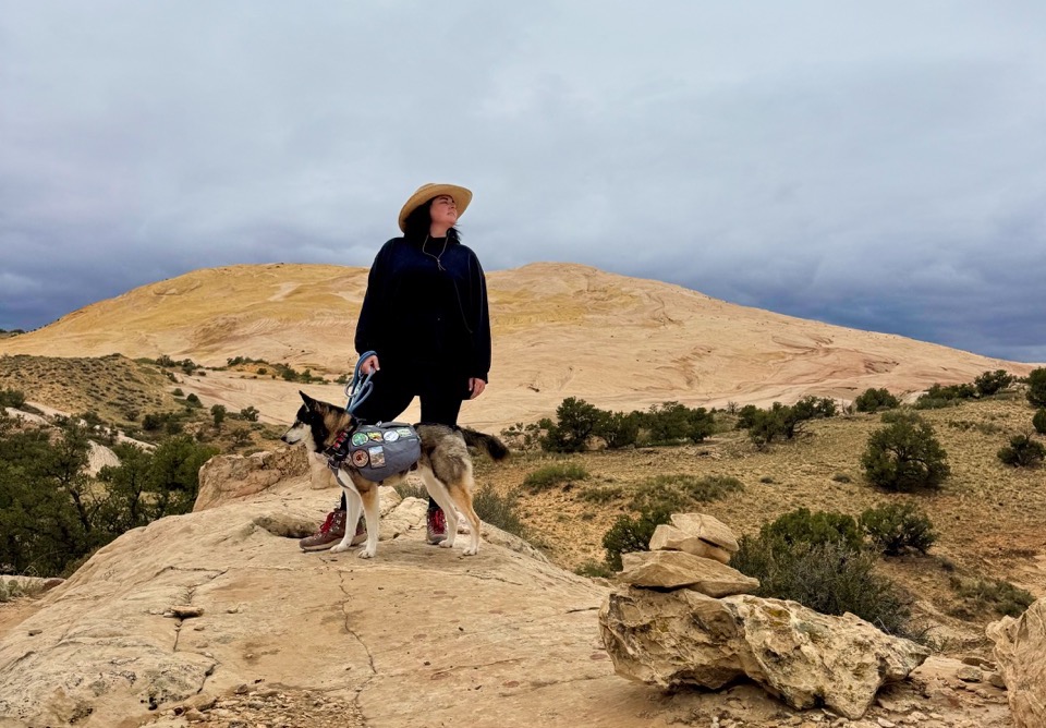 Dog and woman standing in front of large yellow rock landscape in Grand Staircase Escalante, Utah